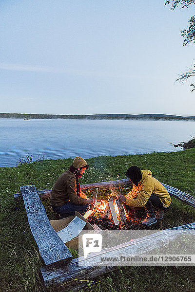 Sweden  Lapland  Two friends preparing a bonfire at the lakeshore