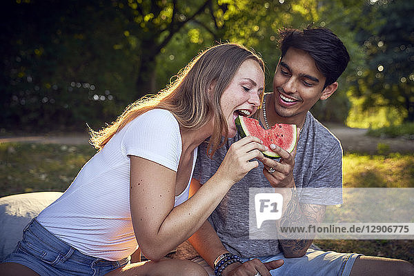 Young couple sitting in park  eating watermelon