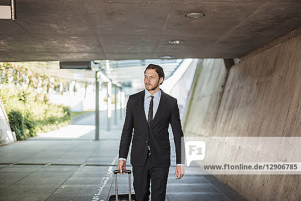 Businessman with rolling suitcase walking in underpass
