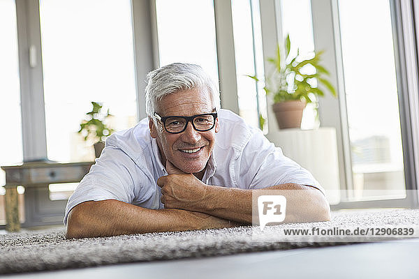 Smiling mature man relaxing lying on carpet at home