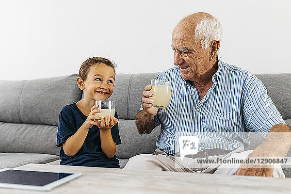 Grandfather and grandson sitting together on couch drinking lemonade