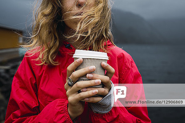 Norway  Lofoten  close-up of young woman at the coast holding takeaway coffee