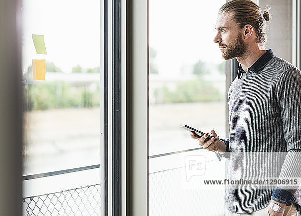 Young businessman with cell phone looking out of window