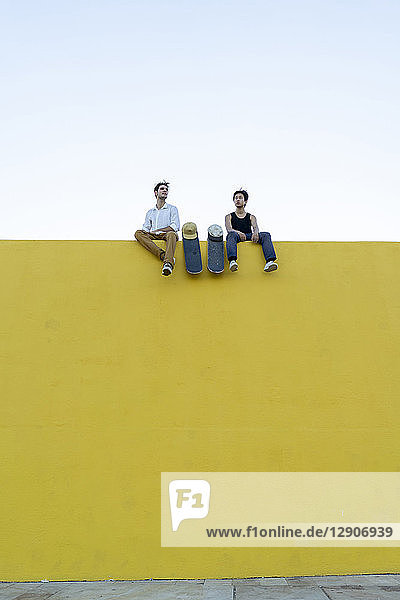 Two young men with skateboards sitting on a high yellow wall