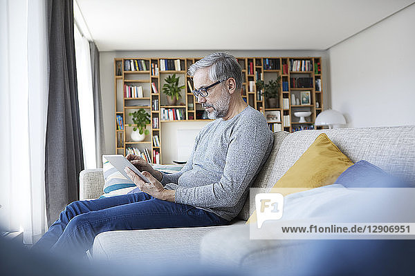 Mature man sitting on couch at his living room using tablet