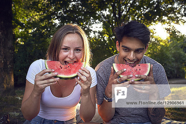 Young couple sitting in park  eating watermelon