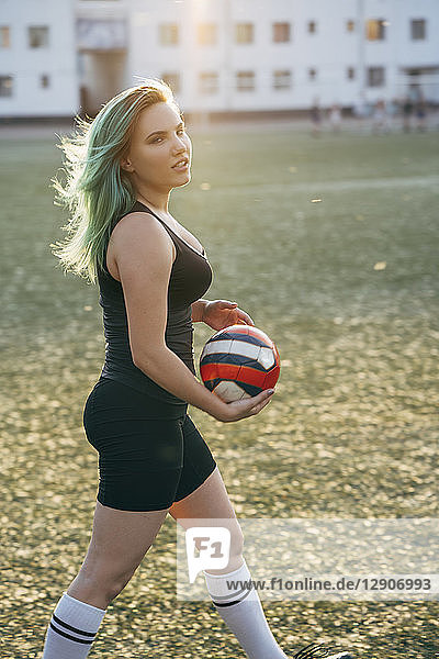 Young woman walking on football ground holding the ball