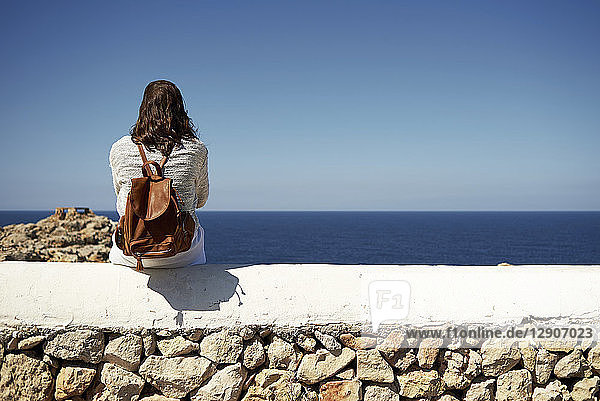 Young brunette woman sitting on wall  looking at view