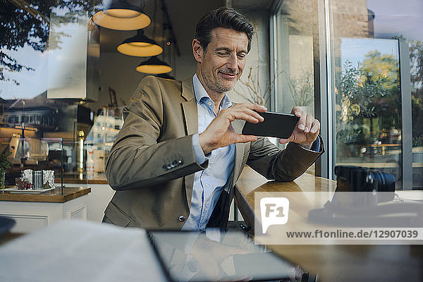 Mature businessman sitting in coffee shop  using smartphone
