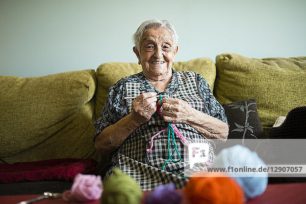 Portrait of smiling senior woman crocheting on the couch at home