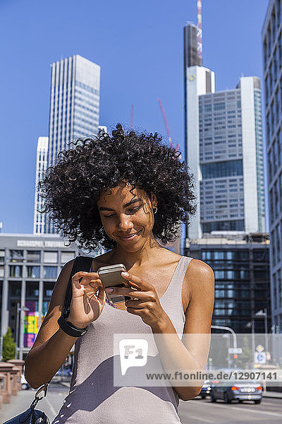 Germany  Frankfurt  portrait of smiling young woman with curly hair using cell phone