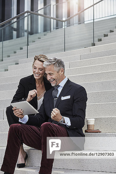 Two business people sitting together on stairs looking at tablet
