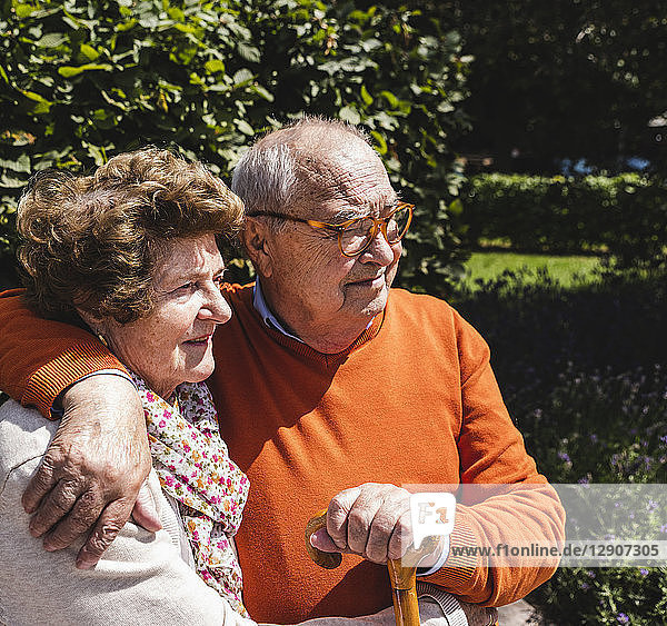 Senior couple sitting on bench in a park  with arms around