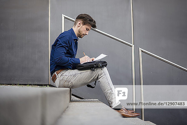 Businessman sitting on stairs outdoors taking notes