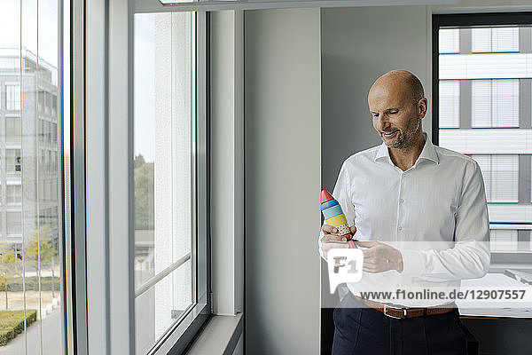 Businessman standing by window  holding toy rocket