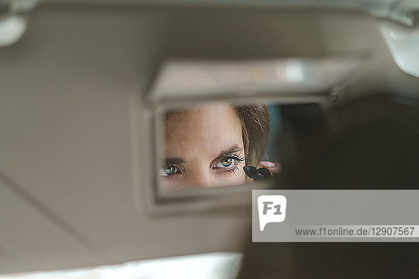 Woman mirrored in rear view mirror applying mascara in car