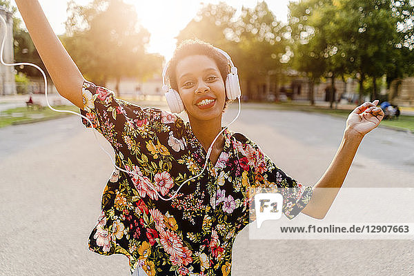 Happy fashionable young woman with headphones dancing outdoors at sunset