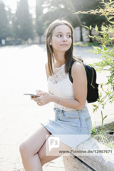 Young woman with backpack and cell phone resting in a park