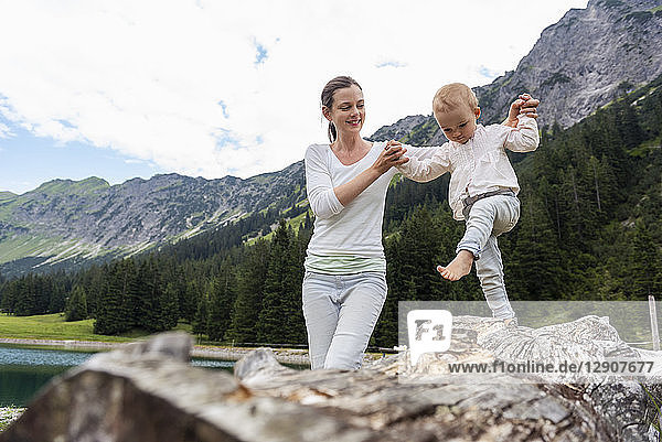 Germany  Bavaria  Oberstdorf  mother helping little daughter balancing on a log