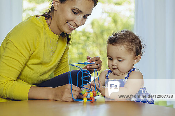 Happy mother and baby daughter playing with motoric loop