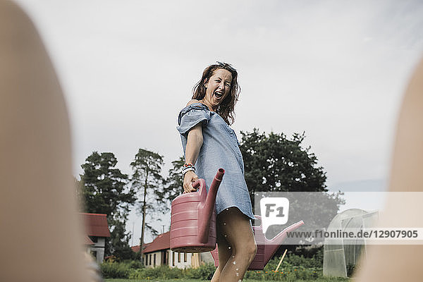 Happy playful woman carrying watering cans in garden