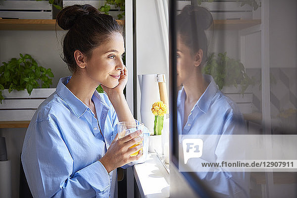 Young woman drinking orange juice in her kitchen