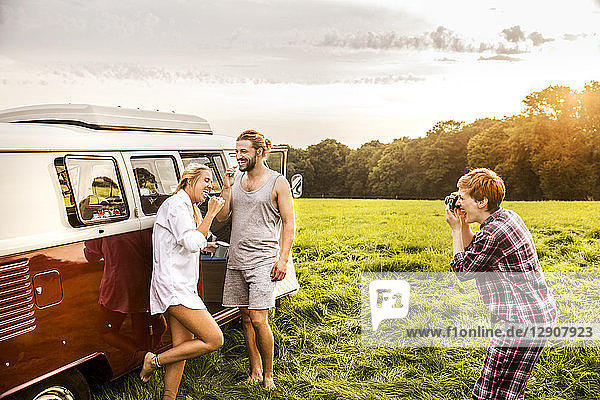 Woman taking picture of friends brushing teeth at a van in rural landscape