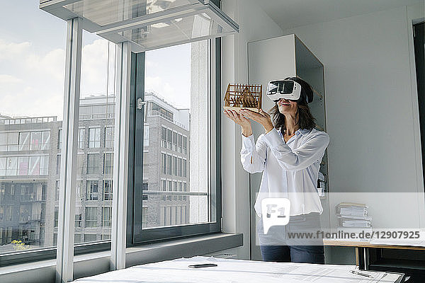 Woman holding architectural model of house  using VR glasses