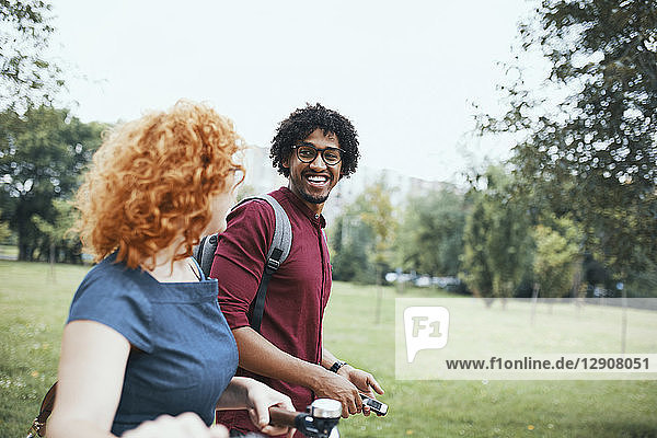 Friends walking in park  talking  woman pushing bicycle