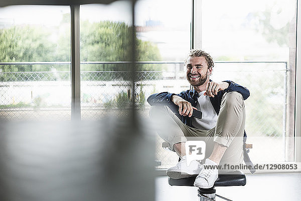 Smiling casual businessman sitting on office chair with cell phone