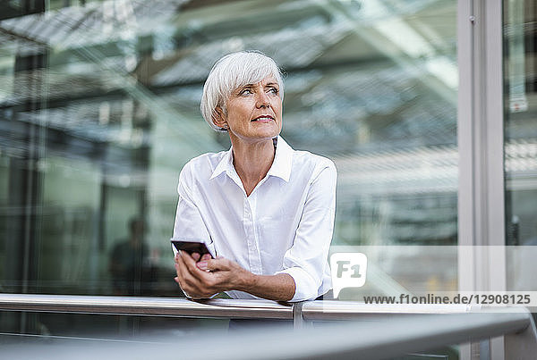 Senior businesswoman leaning on railing in the city with cell phone