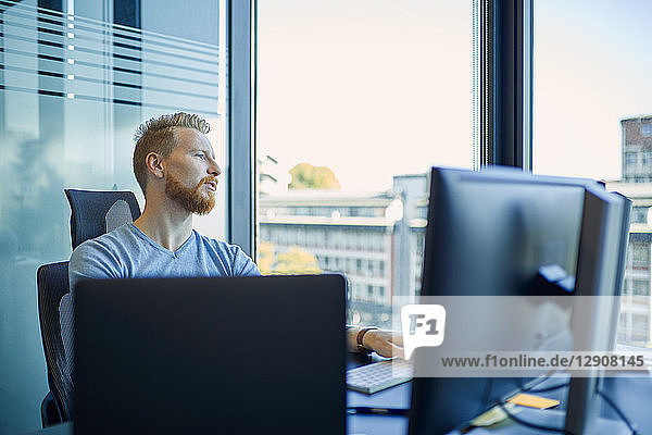 Businessman at desk in office looking out of window