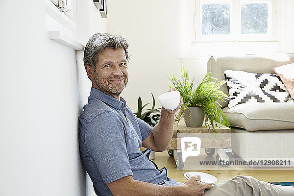 Mature man at home sitting in front of couch  drinking coffee