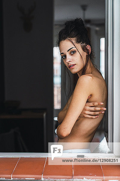 Portrait of beautiful barechested young woman at the window