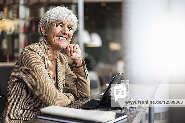 Portrait of smiling senior businesswoman with tablet in a cafe