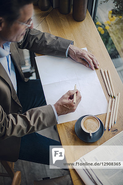 Mature businessman sitting in coffee shop  drawing on paper