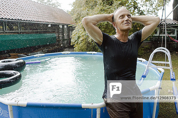 Mature man enjoying summer rain in garden at swimming pool