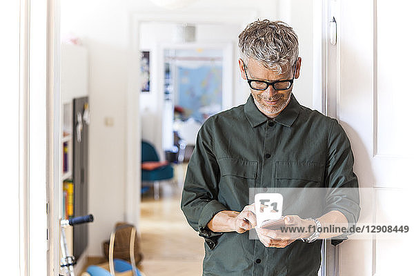 Mature man leaning against door case at home using cell phone