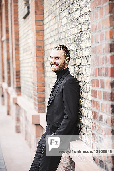 Smiling fashionable young man leaning against brick wall