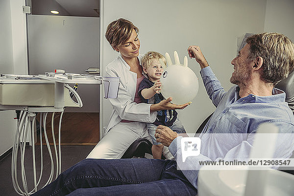 Little boy siting on dentist's lap  playing with a balloon  father smiling