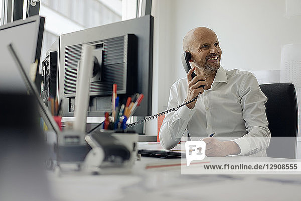 Smiling businessman sitting at his desk  talking on the phone