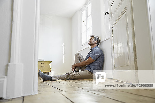 Mature man sitting on floor of his bedroom  daydreaming