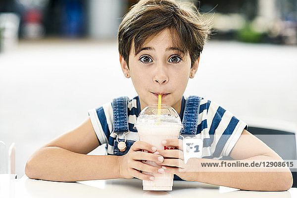 Portrait of little girl drinking strawberry milkshake at pavement cafe