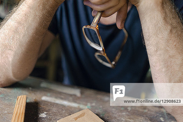 Close-up of man at workbench in workshop holding eyeglasses