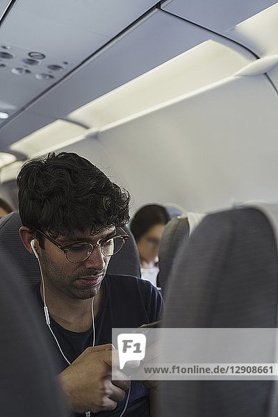 Young man in a plane with cell phone and earbuds