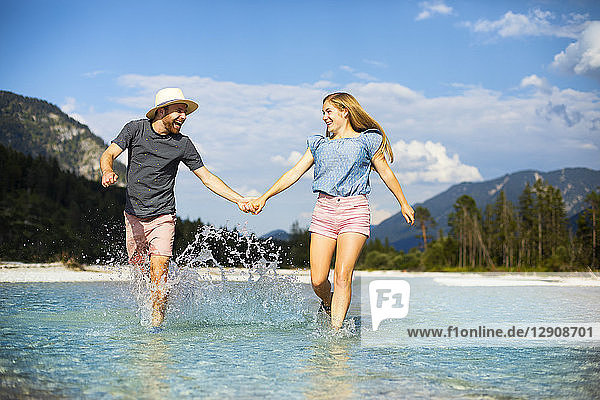 Young couple holding hands and running through water