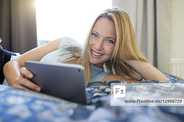 Laughing young woman lying on bed at home  using digital tablet