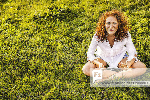 Portrait of happy young woman with tablet relaxing on a meadow