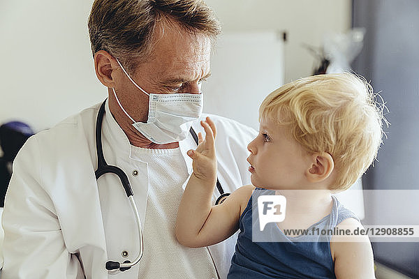 Toddler sitting on lap of pediatrician  wearing protective mask