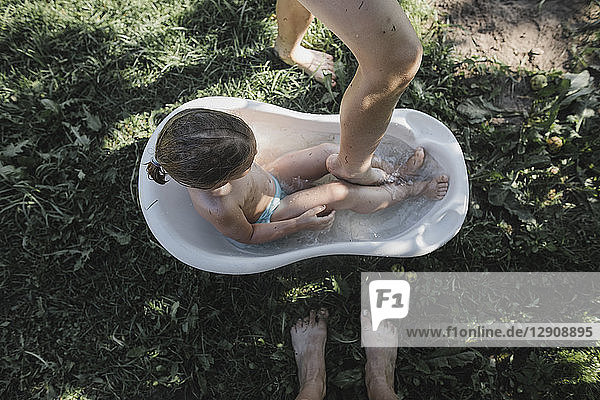 Girl in little bath tub in garden and feet of mother and brother